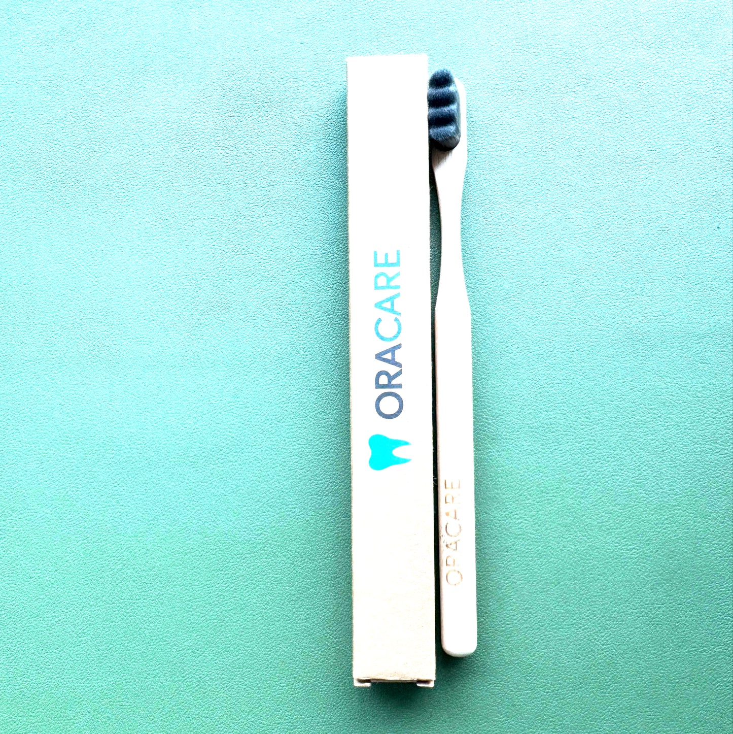 Oracare toothbrush and packaging on a green background