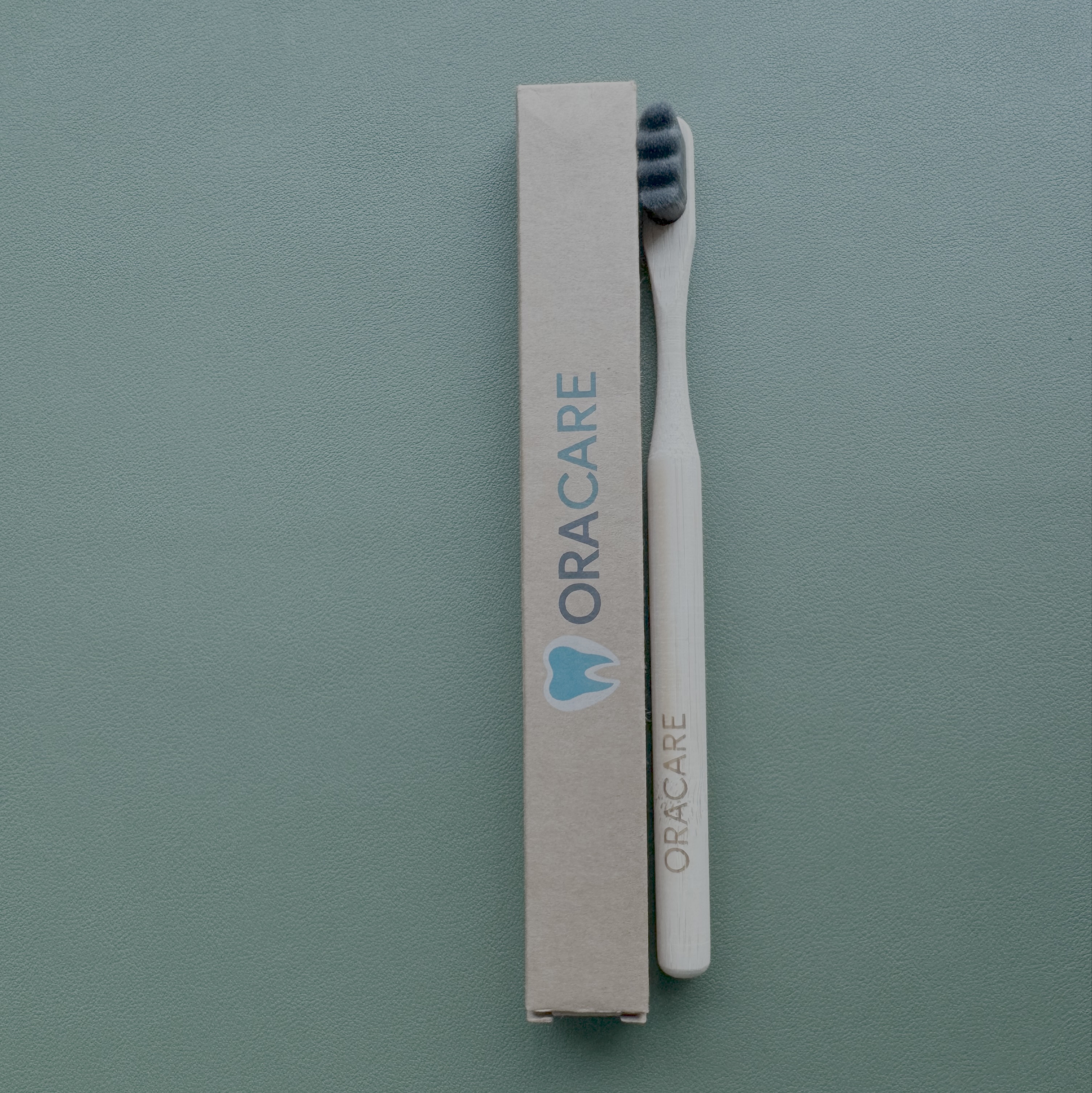 Oracare toothbrush and packaging on a green background